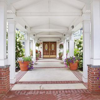 A covered entrance with columns and potted plants leading to a wooden double door.