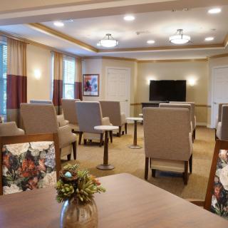 A well-lit community room with arranged seating, tables, and a television.