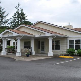 A small residential building with a front porch and surrounding greenery.