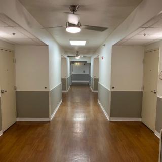 A long hallway with multiple doors, a ceiling fan, and wooden flooring.