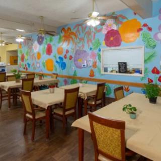 A cozy restaurant interior featuring a vibrant floral mural on the wall, with tables and chairs neatly arranged for dining.