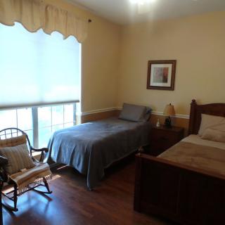 A cozy bedroom with two beds, a rocking chair, and a large window.
