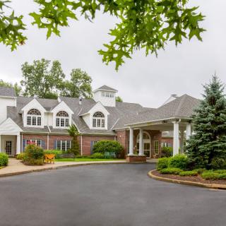 A large residential building with a landscaped entrance and driveway, surrounded by trees.