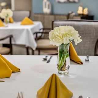 A beautifully set dining table with yellow napkins and a vase of white flowers.