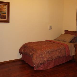 A cozy bedroom with a single bed, wooden floor, and a painting on the wall.