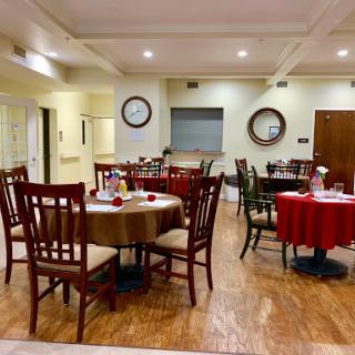 A cozy dining area featuring well-set tables with red tablecloths, surrounded by wooden chairs under warm lighting.
