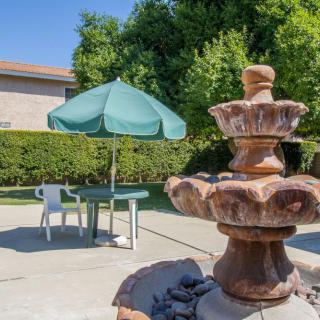 A tranquil backyard scene with a decorative fountain and a patio table shaded by an umbrella.