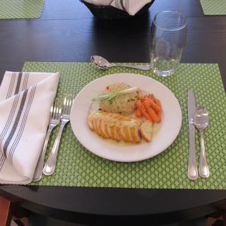 A neatly arranged table setting with a plate of food, including sliced meat and vegetables, on a green polka dot placemat.
