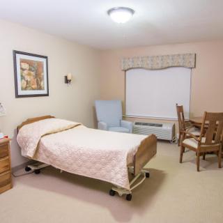 A well-lit healthcare room featuring a bed, chair, and wooden furniture that creates a comfortable atmosphere.