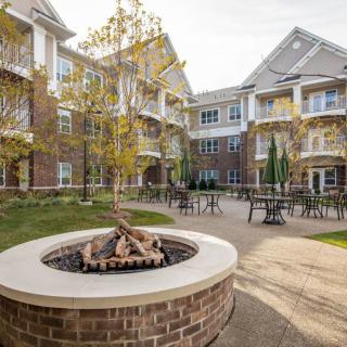 A scenic courtyard with a fire pit surrounded by tables and chairs, nestled within an apartment complex.