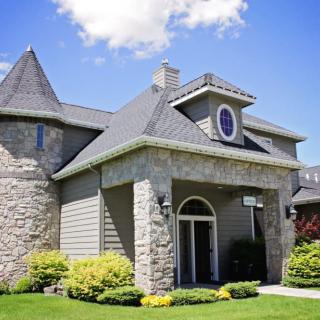 A beautiful stone house with a well-maintained lawn and landscaping under a clear blue sky.