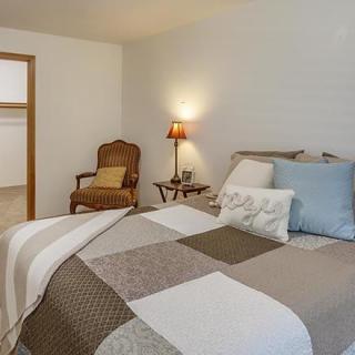 A cozy bedroom with a quilted bedspread, a side table with a lamp, and an upholstered chair.