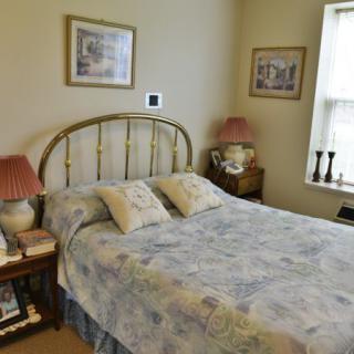 A cozy bedroom with a neatly made bed, decorative lamps, and framed artwork on the walls.