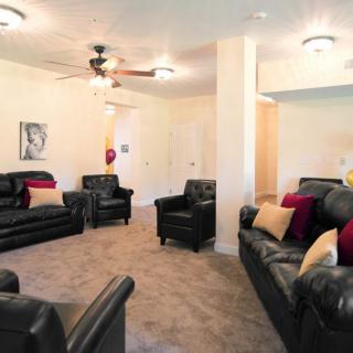 A cozy living room with multiple black leather sofas and colorful throw pillows, featuring a ceiling fan and carpeted floor.