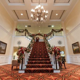 A grand staircase in a decorated lobby, adorned with festive garlands and a chandelier above.