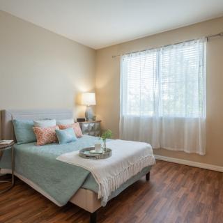 A cozy bedroom with a neatly made bed, soft lighting, and a window letting in natural light.