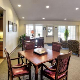 A well-lit interior space featuring a wooden dining table with chairs, surrounded by large windows and tasteful decor.
