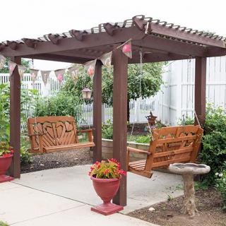 A charming wooden pergola with swings and potted plants in a garden setting.