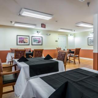 A cozy dining area with tables set with black and white tablecloths, surrounded by comfortable chairs, and illuminated by overhead lighting.