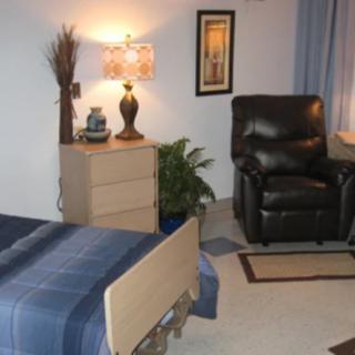 A cozy bedroom with a bed, recliner chair, and dresser under warm lamp lighting.