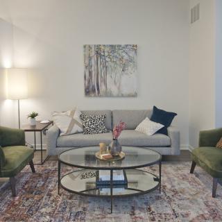 A stylish living room with a cozy sofa, two armchairs, and a glass coffee table, complemented by a decorative rug and wall art.