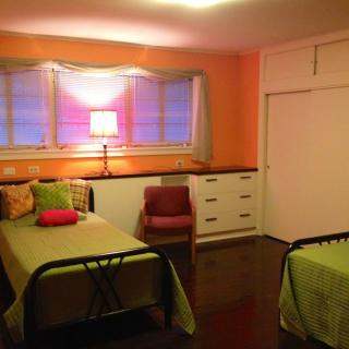 A cozy bedroom with twin beds, vibrant pillows, and a warm orange wall.