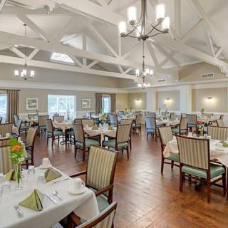 An elegant dining room with neatly arranged tables and chairs, featuring chandeliers and a high ceiling.