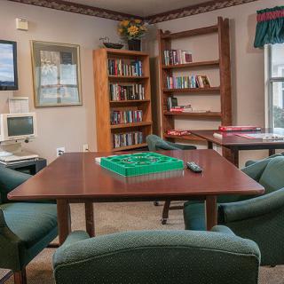 A cozy library with bookshelves, a computer, and a seating area featuring a table ready for a game.