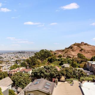 A scenic view of a hilly landscape overlooking an urban area with houses and greenery under a clear blue sky.