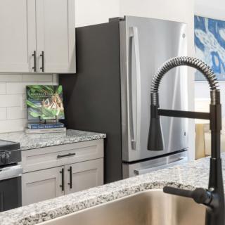 A modern kitchen with a stainless steel refrigerator, granite countertops, and a stylish faucet.