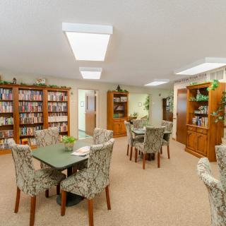 A cozy library room with bookshelves, tables, and chairs.