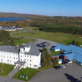Aerial view of a large building surrounded by fields and trees with a lake in the background.