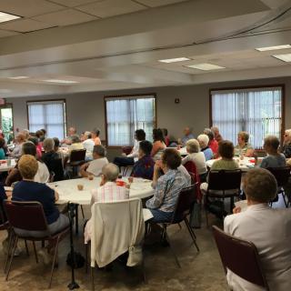 A community gathering with people seated around tables indoors.