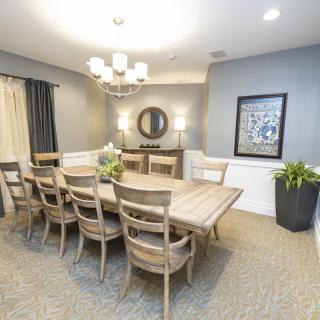 A well-decorated dining room with a large wooden table and chairs, illuminated by a chandelier.
