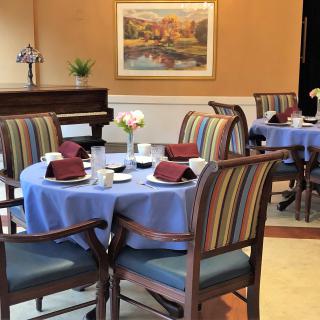 A neatly set dining area with tables and chairs, featuring a piano and artwork on the wall.