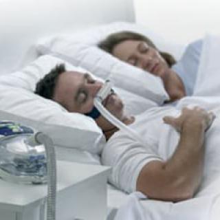 A man sleeping with a CPAP machine alongside his partner in bed.