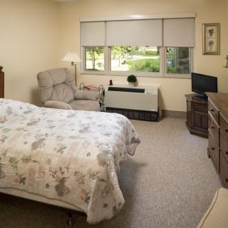 A cozy bedroom with a bed, armchair, and a small television, featuring a window with a view outside.