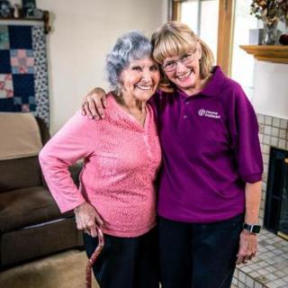 Two women smiling and embracing in a cozy living room setting.