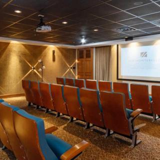 An empty theater room with rows of seats facing a projection screen.