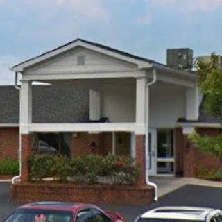 A view of a building entrance with a covered porch and surrounding parking.