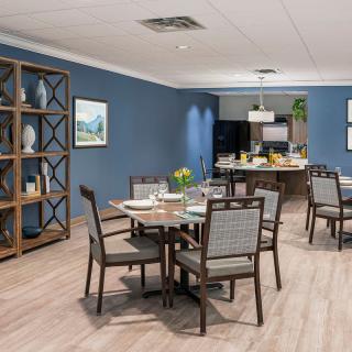 A modern dining room with blue walls, neatly set tables and chairs, and a stylish shelving unit.