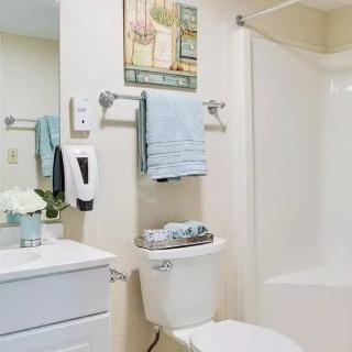 A clean and neatly organized bathroom with white fixtures, blue towels, and light decor.