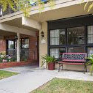 A cozy residential building with a porch, featuring a red bench and potted plants along the pathway.