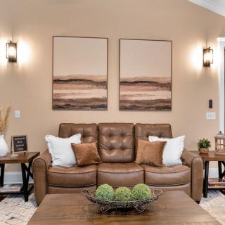 A cozy living room with a brown leather sofa, adorned with pillows and complemented by wall paintings and elegant lighting.
