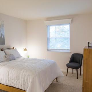 A minimalist bedroom with a neatly made double bed, a window, and a chair.