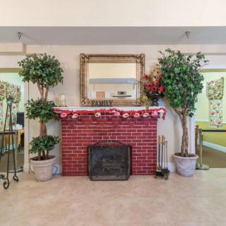 A cozy living room with a red brick fireplace decorated with plants and a large mirror above.