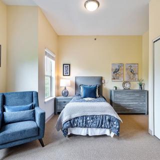 A cozy bedroom with a single bed, blue armchair, and decorative elements.