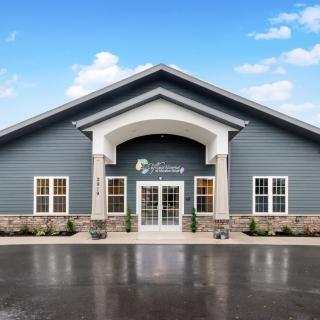 A modern building with a stone and siding exterior, featuring large columns at the entrance under a clear blue sky.