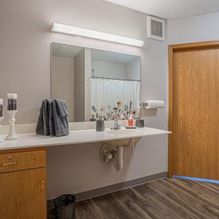 A modern bathroom with a large mirror, sink, and various toiletries on the countertop.