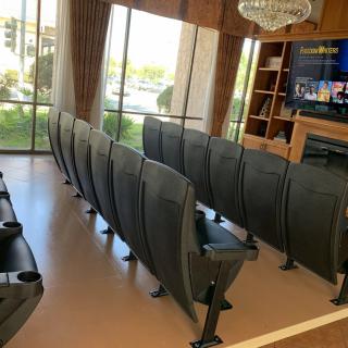 A luxurious home theater room with multiple rows of comfortable seating facing a large screen TV.